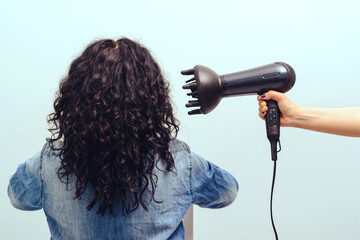 Woman styling her curly hair with hairdryer with special diffuser nozzle.