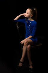 Portrait of a little girl sitting on an old Viennese chair, black background.