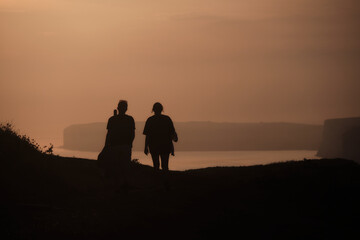 Silhouette of a couple walking into the sunset with seven sisters cliffs in the distance