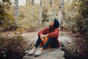 Young woman sitting on a small wooden bridge in the forest