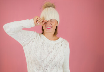 Nice woman with rose hat and blonde hair touching it while smiling at camera on a pink background with empty space