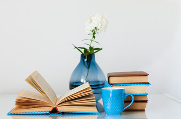 Cozy home interior decor: stack of books, cup of coffee and vase with white flower on a glass table. Distance home education.Quarantine concept of stay home.