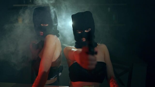 The girls robbers in a black masks and sexy suit with pistols and cash aims at the camera. Bag with money. Role-playing games