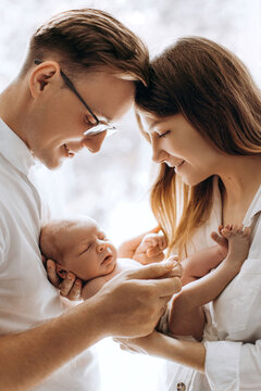 Happy young parents with newborn baby girl, loving mom hold little daughter in arms, caring dad gently hold a hand of adorable baby girl, tender family moments, parenting concept