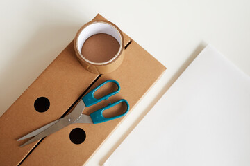 High angle view of cardboard box with adhesive tape and scissors on it isolated on white background
