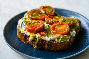 Healthy Toast Tartine with Cream Vegan Cashew Cheese Truffle Flavored, Pesto Sauce and Cherry Tomatoes.