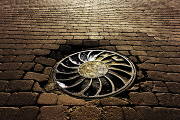 Metal sewer hatch. Round cover of storm drain on a stone road.