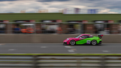 Fototapeta na wymiar A panning shot of a pink and green racing car as it circuits a track.