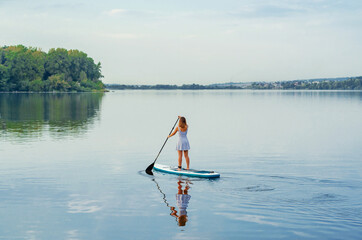 Woman in a dress on a sap board floats on the blue water of the