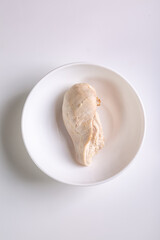 Boiled chicken breast fillet is in a white plate on a white background. View from above. Vertical...