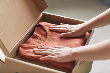 Close-up of woman opening parcel with new red shirt she getting her online order