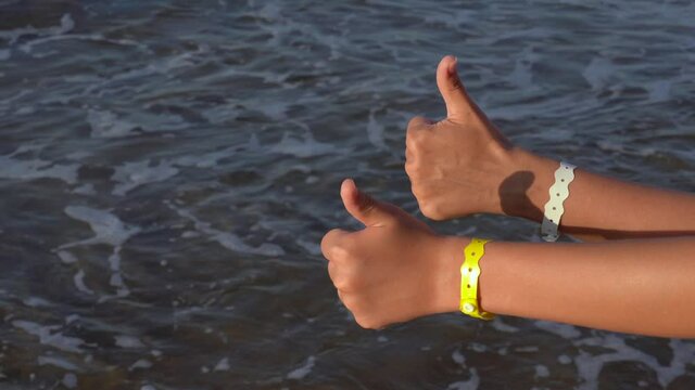 Closeup view 4k video of two hands of happy people standing on sunny morning beach of hotel resort. Mom and her son show thumbs up cheerfully as sign of like and approval.
