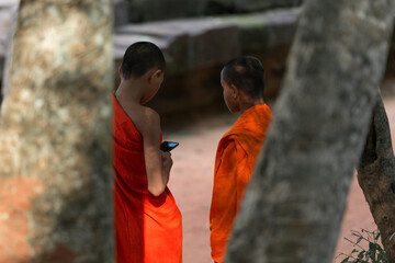Focusing on unidentified two monks is using the mobile phone at Ta Prohm Temple, Siem Reap, Cambodia.
