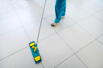 Floor washing in the mall. A woman is cleaning tiles in a large room. Cropped frame. No face