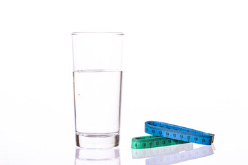 Glass of pure natural water and Two stacked colorful measuring tapes isolated on white background. Symbol of diet for loosing weight. Water is source of health and wellness.