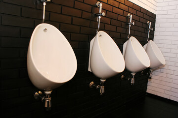 Modern white urinals in a men's public restroom on a decorative brick wall