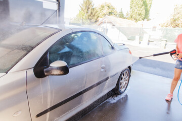 Washing car with pressure washer at self-service car wash station