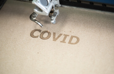 Industrial laser engraving word "covid" on a cardboard, close up view