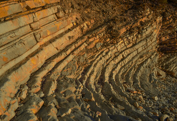 Layered sandy red orange light twisted cliffs made of stone bricks on Black Sea coast, in Blue Bay (Golubaya Bay), near Gelenzhik. Summer sunset on shore