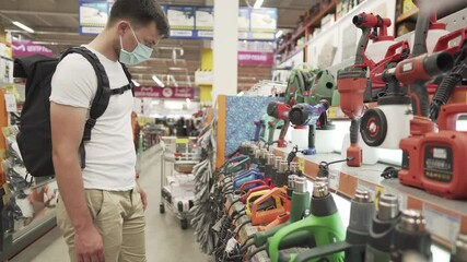 Customer look at the goods in diy shop, shopping in building supermarket. The buyer chooses tool for repair on store shelves. Man shopping electric tool at hardware store. Sale of electric tools