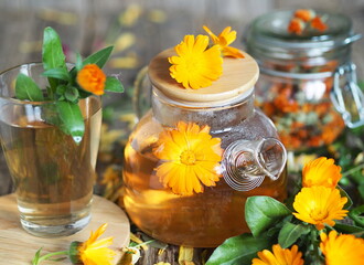 Medicinal autumn background. Herbal healthy marigold tea with a teapot, dried and fresh flowers on an autumn wooden background.