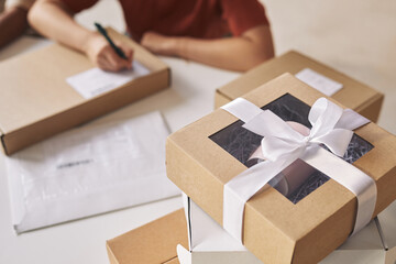 Close-up of parcel packed in cardboard box with ribbon on the table with woman working in the...