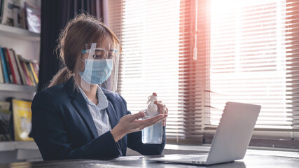 Businesswoman with face mask and Face shield using hand sanitizer while cleaning her hands in the office. Working from home, Woman  wearing protective mask. Corona virus protection.
