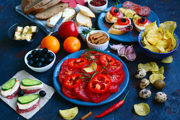 Various snacks, sandwiches, tomatoes, olives, bread on a dark table, closeup. Healthy snacks concept