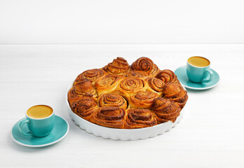 Homemade cinnamon rolls from yeast dough and two cups of coffee espresso on white wooden table. Copyspace.