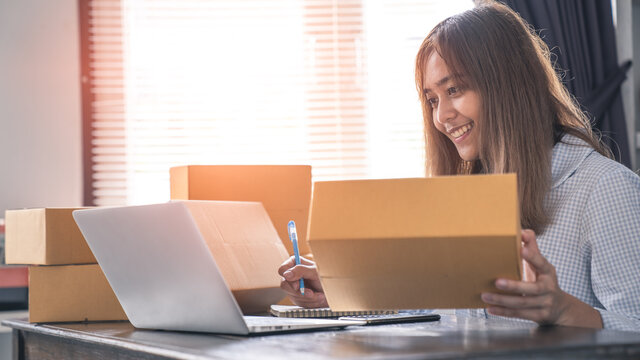Asian business woman working online e-commerce shopping at her shop. Young woman seller prepare parcel box of product for deliver to customer. Online selling, e-commerce.
