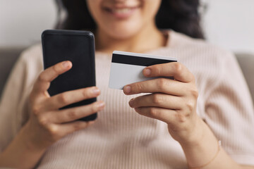 Close-up of young woman using her mobile phone to pay online with credit card