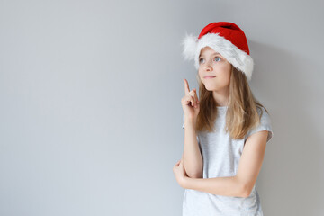 Portrait of a blonde caucasian pensiv girl in a Santa hat on a grey background. Christmas and happines concept. Close up, copy space