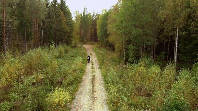 Motorcyclist driving towards the camera on a small gravel road in the forest. No camera movements, filmed in 4K.