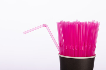 Pink plastic straws in black disposable paper cup isolated on white background. One flexible straw...