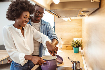 Cute joyful couple cooking together and adding spice to meal, laughing and spending time together...