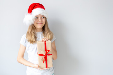 Portrait of a blonde caucasian smiling girl in a Santa hat holding the gift in her hands on a grey background. Christmas and happines concept. Close up, copy space
