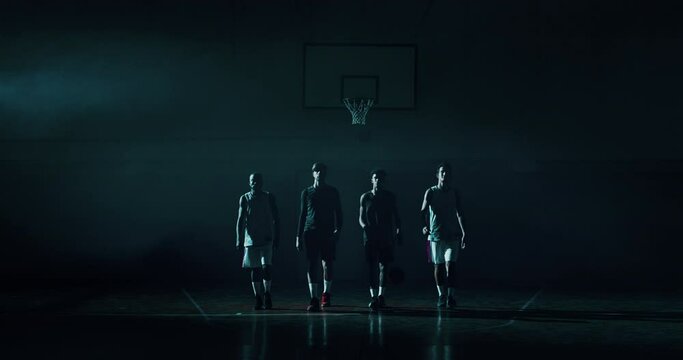Cinematic slow motion shot of young professional male players are walking towards a camera before to start practicing a basketball work out in a gym.
