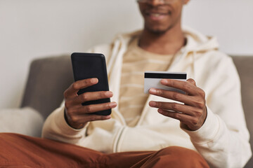 Close-up of African man holding mobile phone and credit card and paying for bills online sitting at home