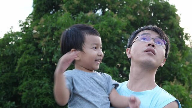 4K Asian child boy and dad in happy moment shot, smiling and laughing with happy cute face outdoor. Son in hug of father. Father's day and relationship concept. Real person in authentic scene.