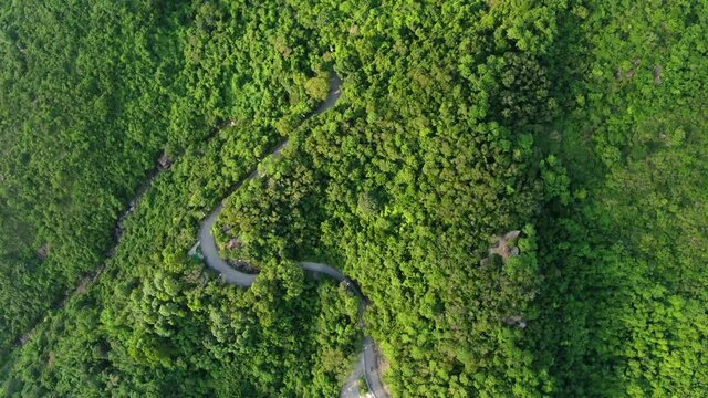 Aerial view of a narrow winding mountain road surrounded by lush green nature.