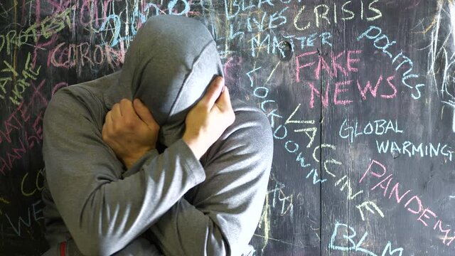 Anxious depressed man cover face in fear, negative words and News headlines written on wall