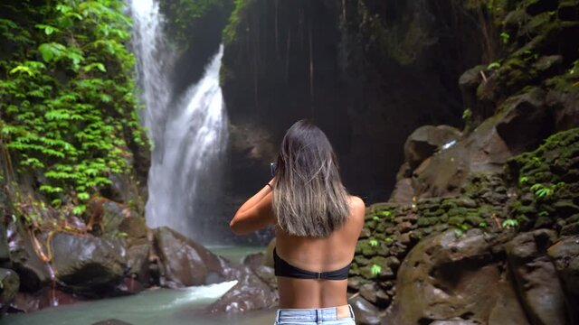 Beautiful young girl photographing scenic view of waterfall, Bali