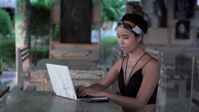 Young freelancer girl typing on laptop searching for inspiration at beach, Bali
