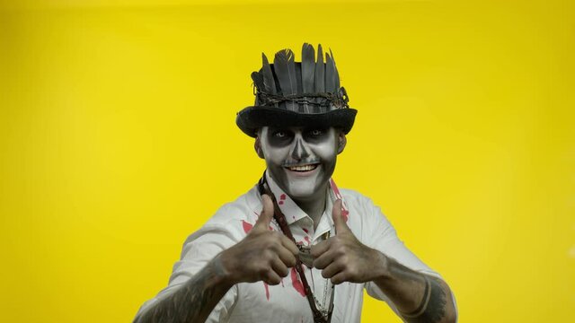 Frightening man in skeleton Halloween cosplay makeup looking at camera, showning thumbs up gesture