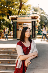 Young brunette woman wearing a dress and a sweater, on city streets on autumn day.