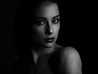 Beautiful mysterious woman in darkness looking dramatic on black background with empty copy space. Closeup portrait.