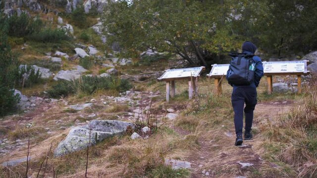 Man with a blue jacket and a backpack, hiking on a rocky trail, on a cloudy, autumn day, in Bulgaria - Handheld, slow motion view