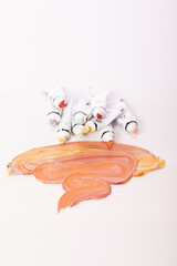 lot of open tubes of multicolored acrylic paint lies on glass table. Wide strokes of paint in...