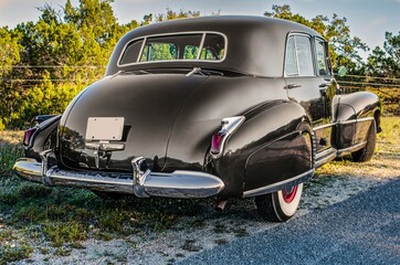 Rear view of classic, vintage luxury car with chrome bumper, chrome fender fin, and wheel covers