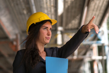 Absorbed woman engineer wearing a yellow protective hardhat pointing upwards on construction site